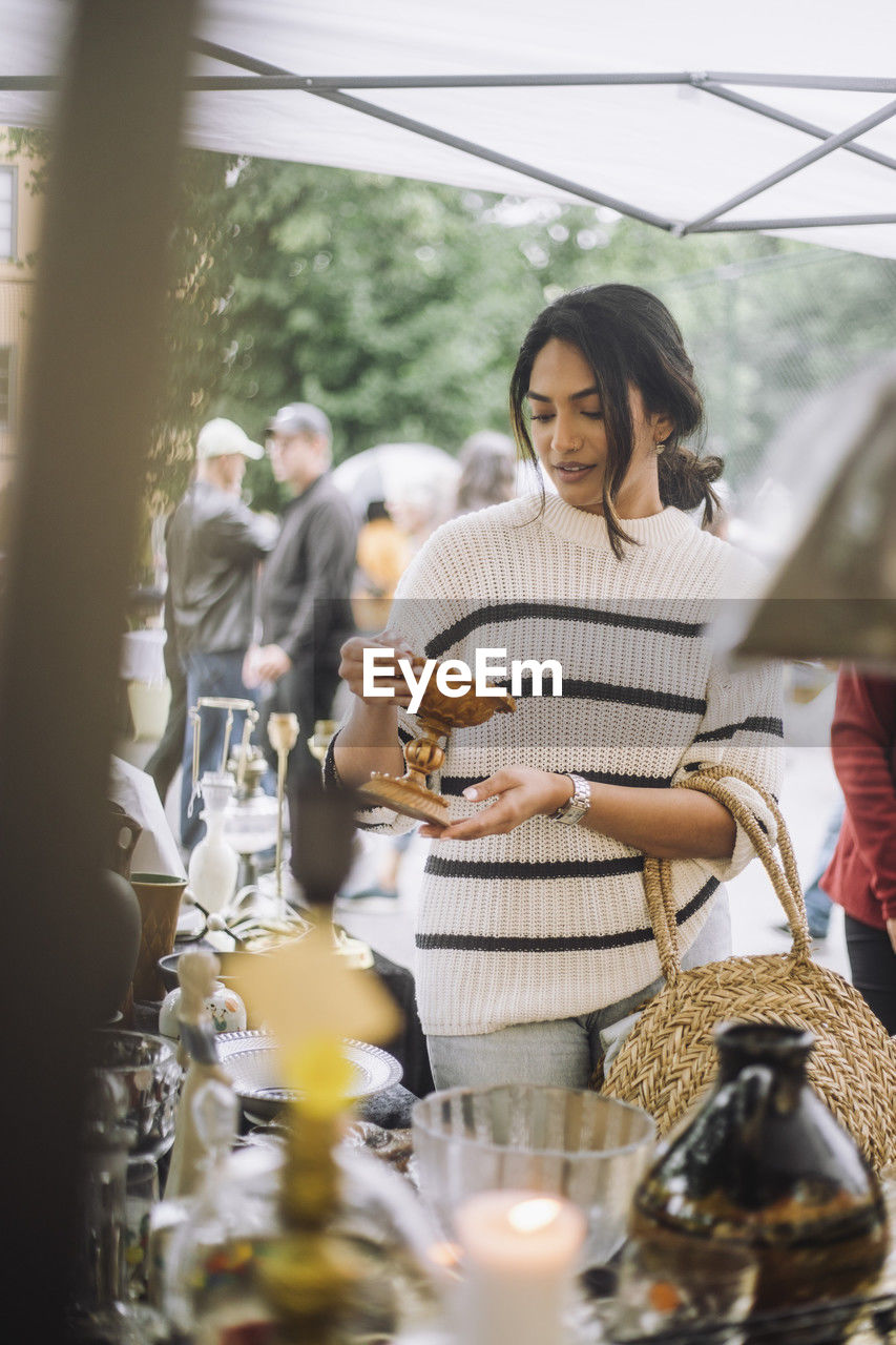 Young woman buying antique standing near stall while doing shopping at flea market