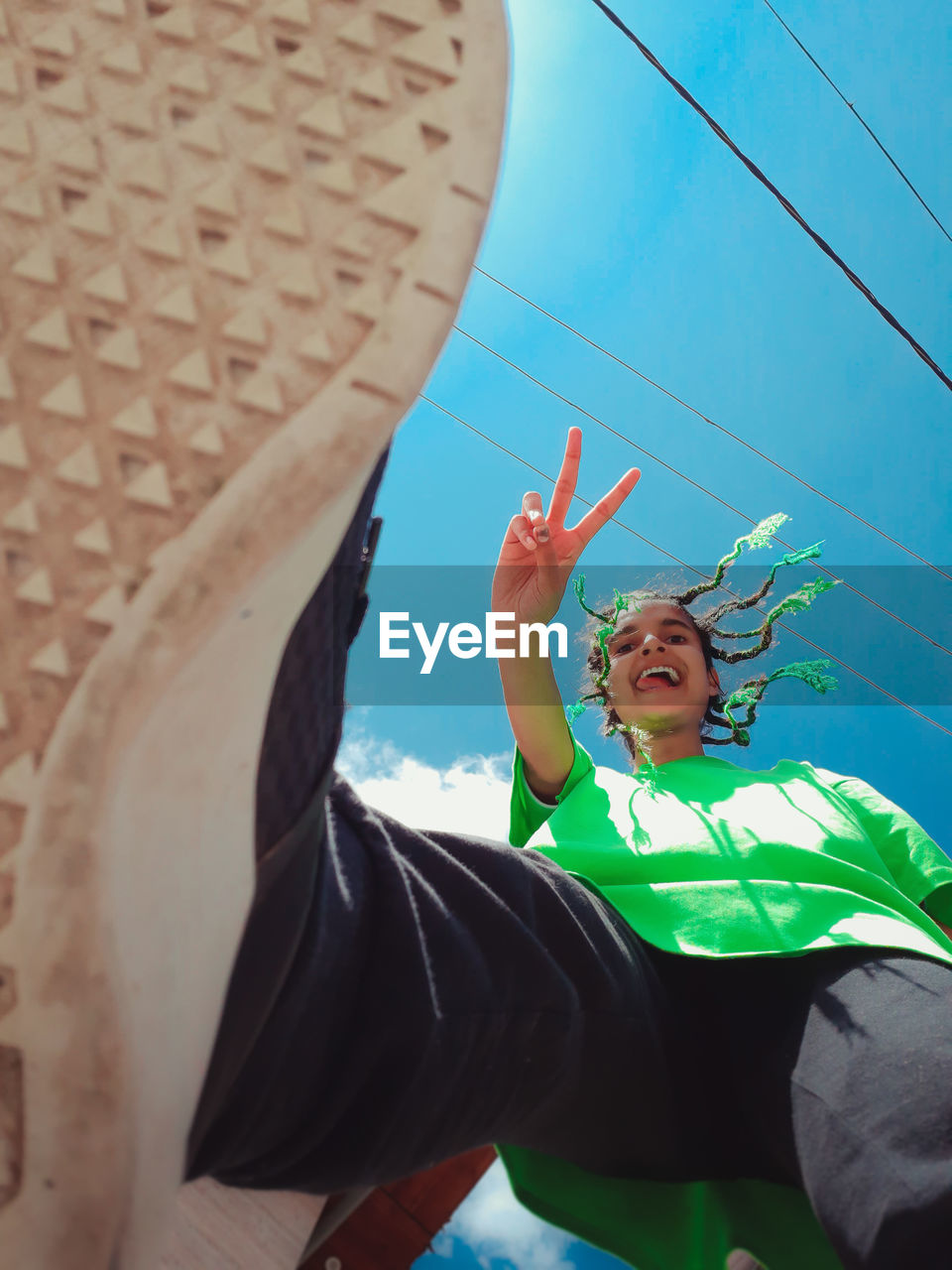 Low angle portrait of cheerful young woman with braided hairstyle against sky