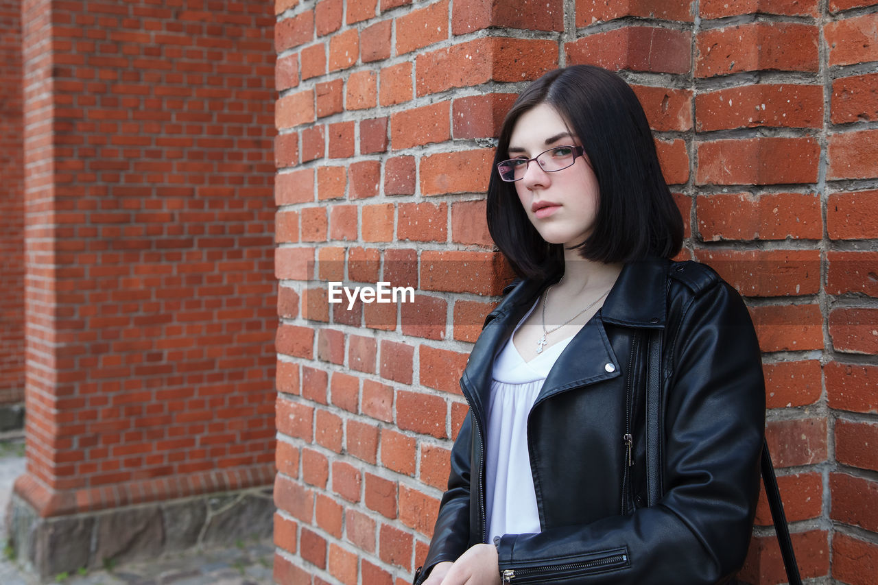 Young beautiful brunette girl in black jacket and  stands near wall of gothic church on summer