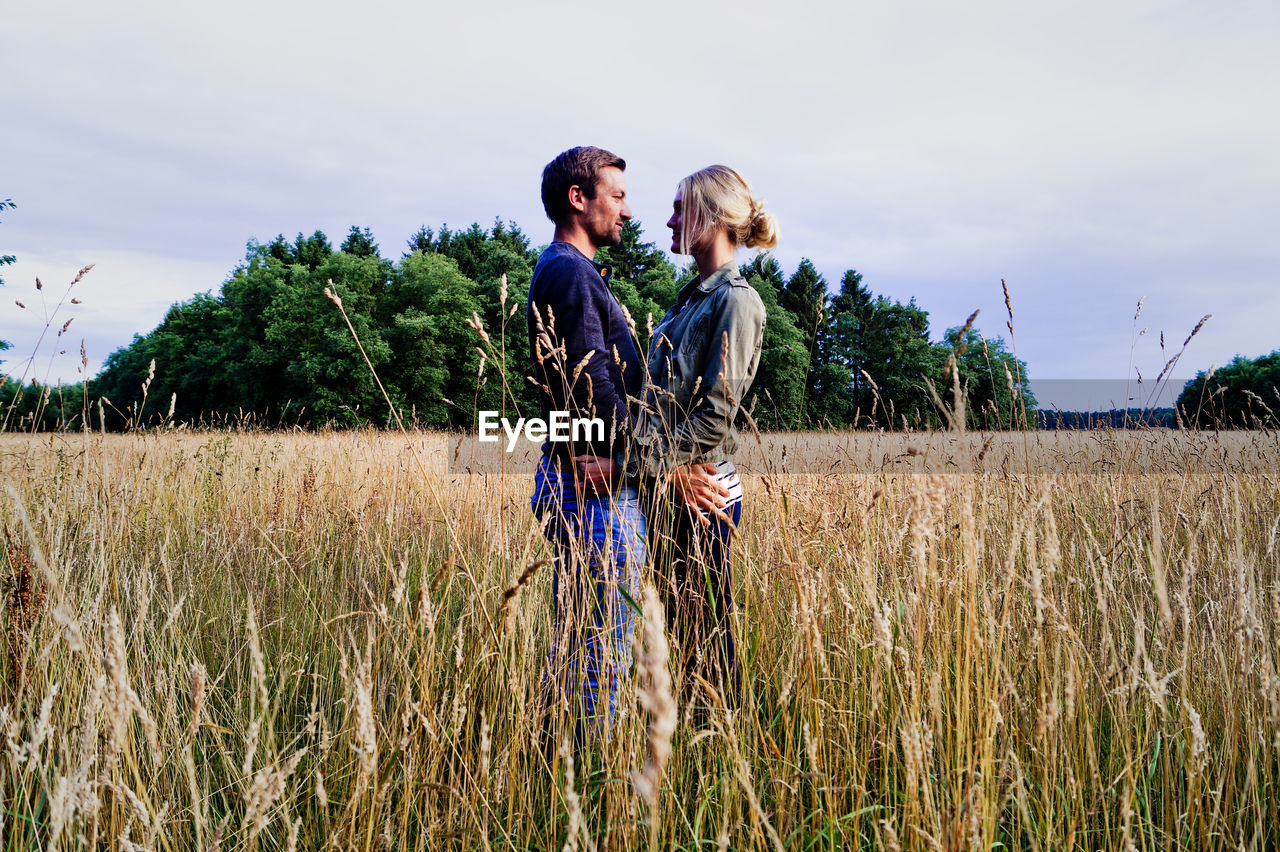 Happy couple standing on grassy field against sky