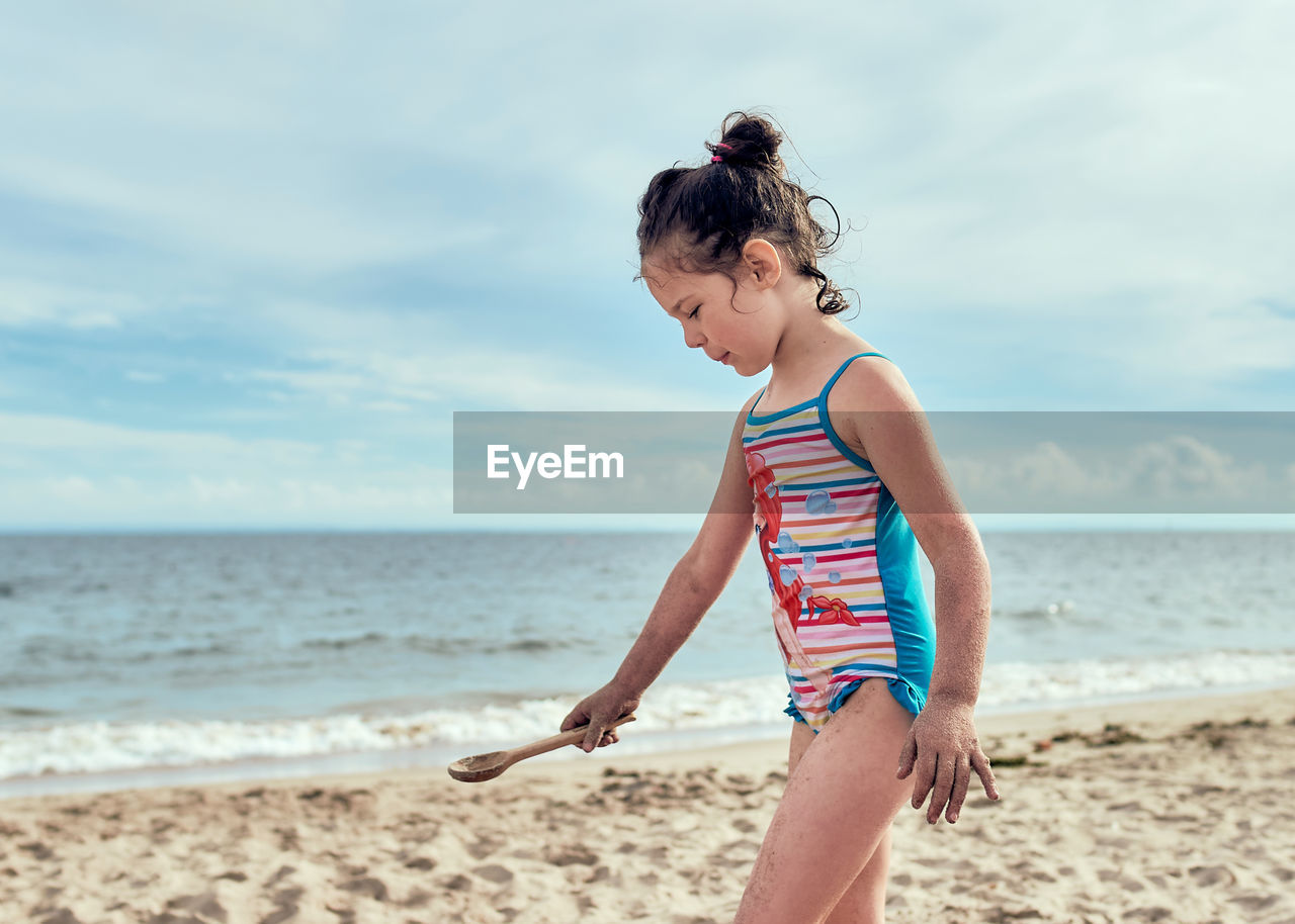 Young girl in a bathing suit is playing with toys at the beach