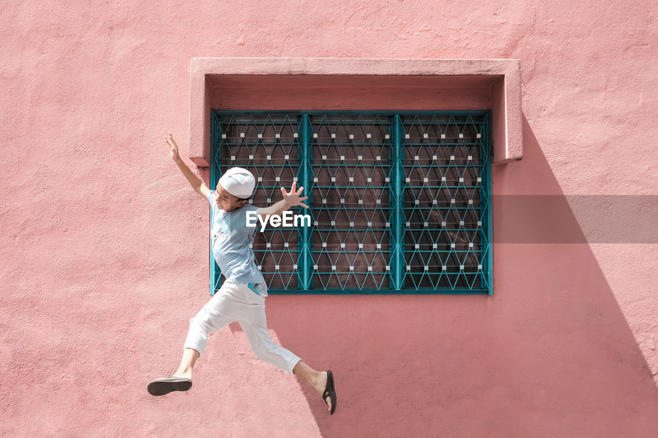 Full length of smiling boy jumping standing against wall