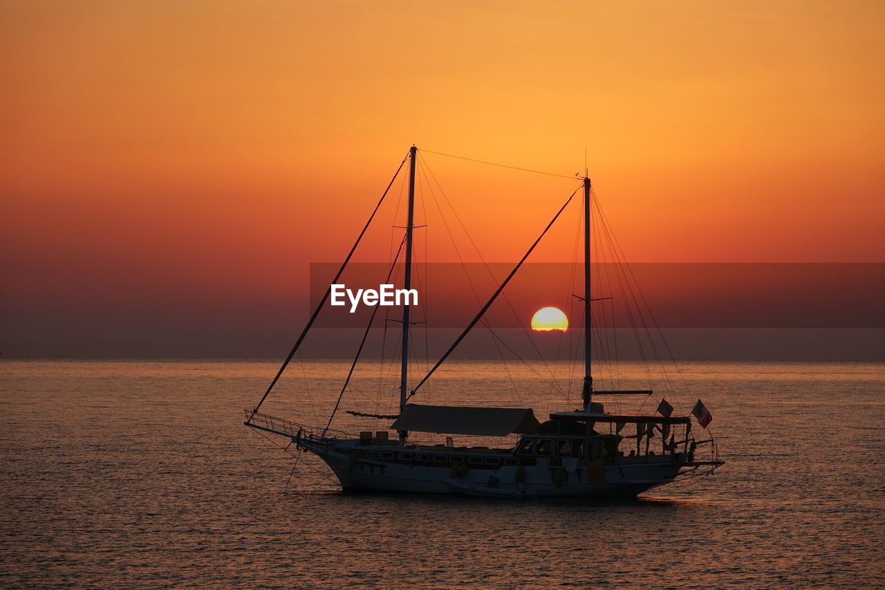 Sailboat in sea against orange sky