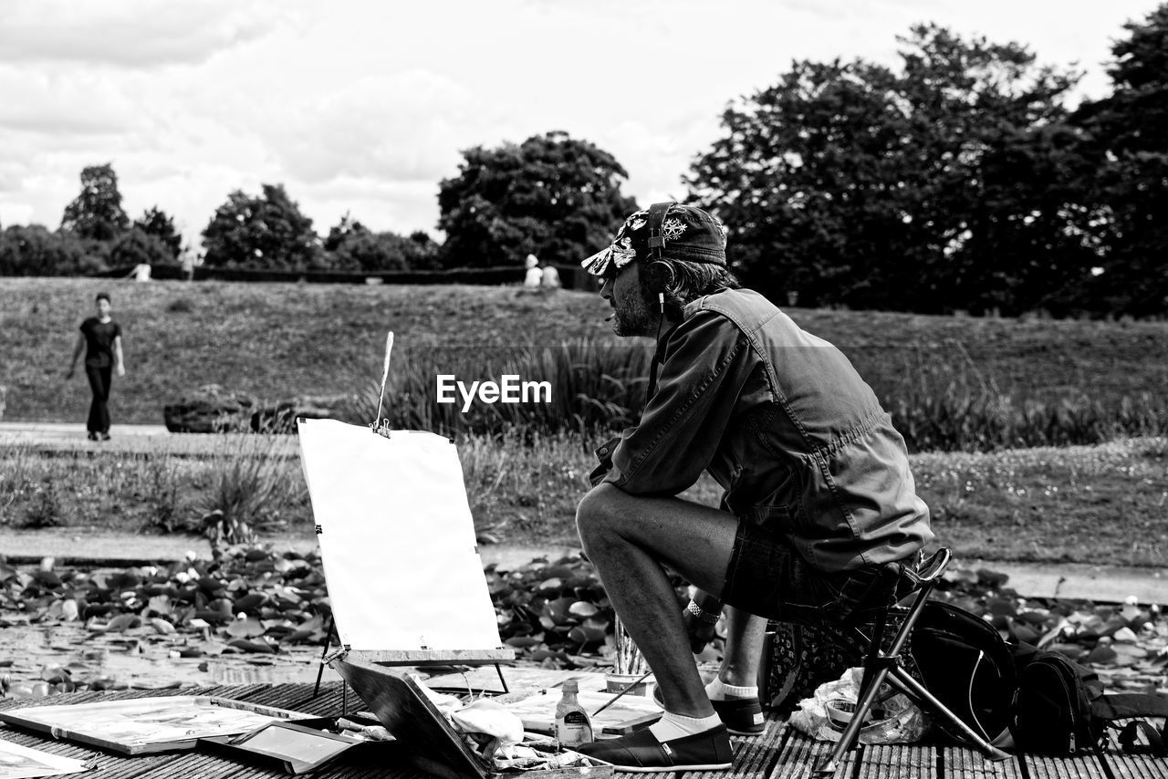 MAN SITTING ON FIELD AGAINST TREES