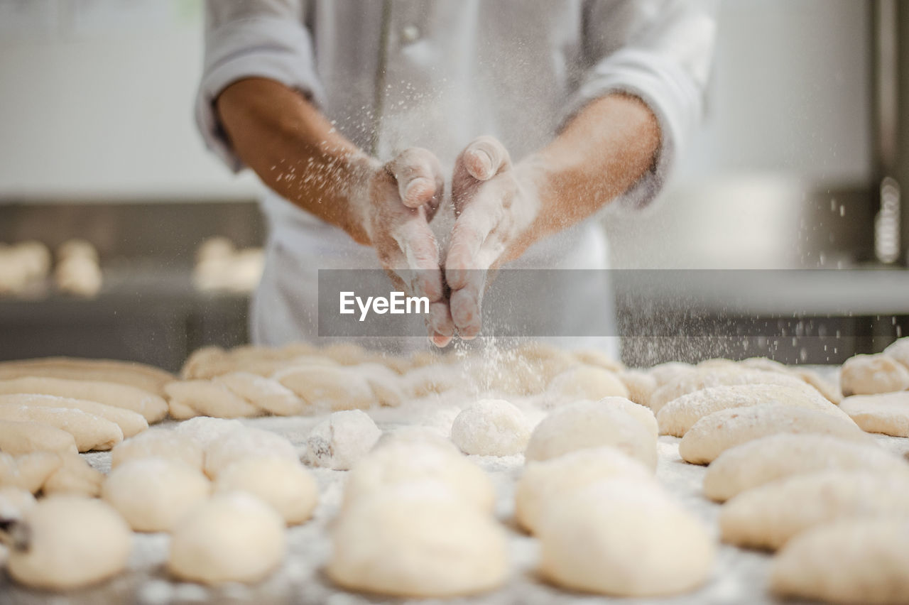 Midsection of chef sprinkling powdered sugar on dough in kitchen