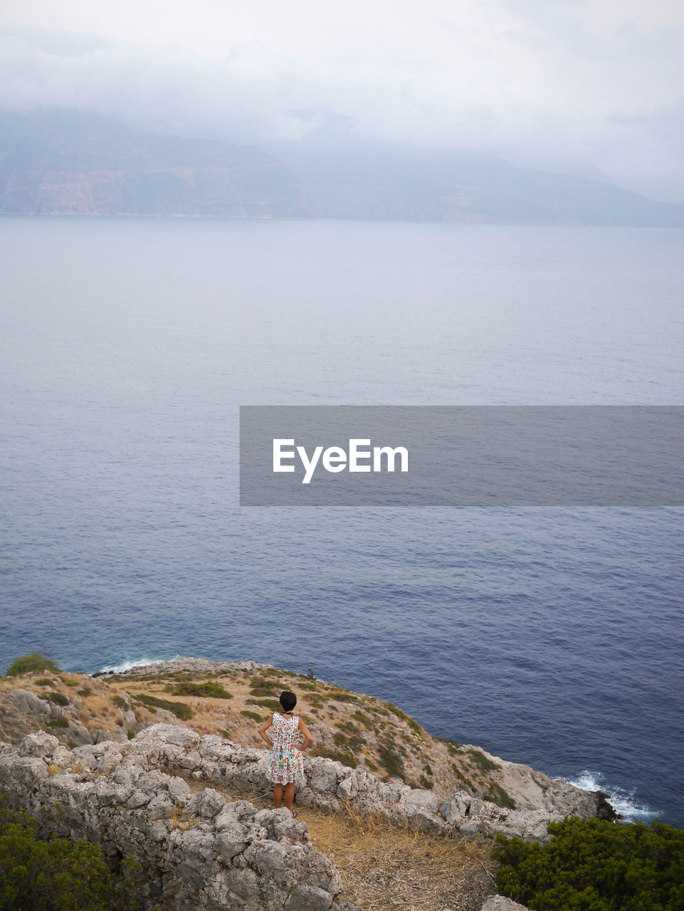 Rear view of woman standing on cliff in front of sea