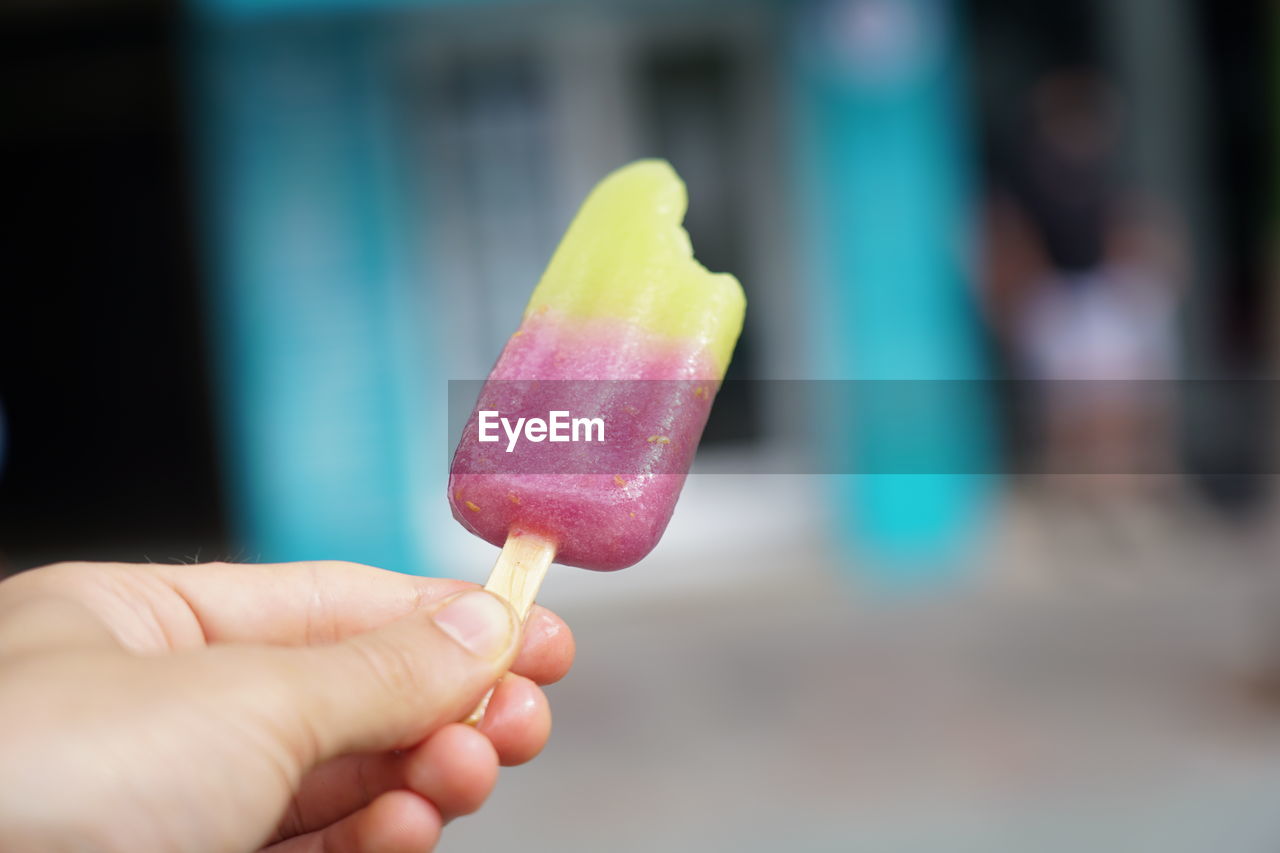 CLOSE-UP OF HAND HOLDING ICE CREAM CONE OUTDOORS