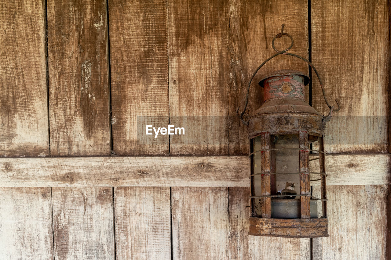 Close-up of old lamp against weathered wooden wall