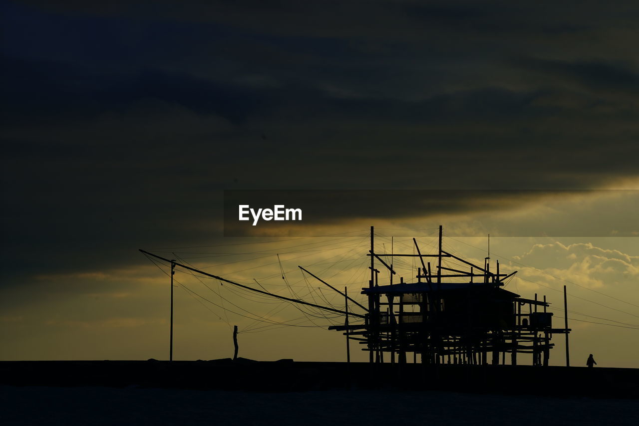 Silhouette stilt houses against cloudy sky at dusk