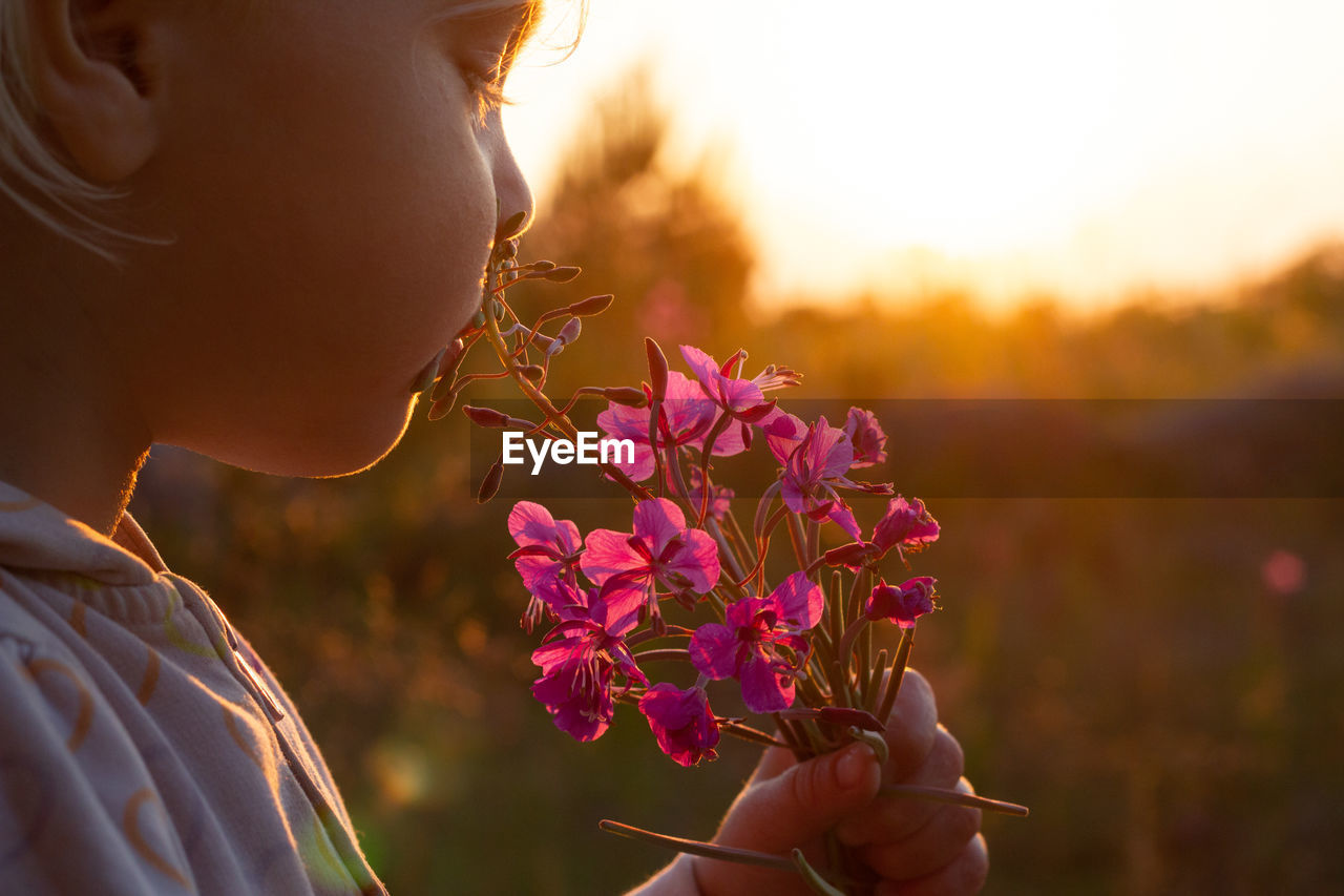CLOSE-UP OF WOMAN HOLDING FLOWERING PLANT AT SUNSET