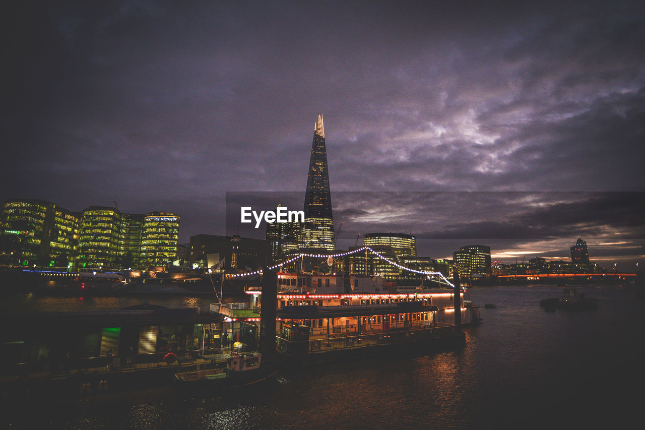 Illuminated city by river against sky at night