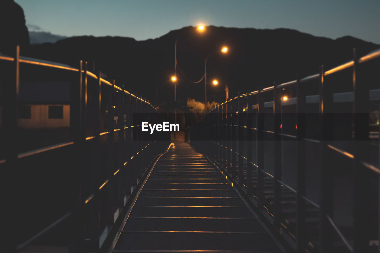 Illuminated footbridge against sky at night