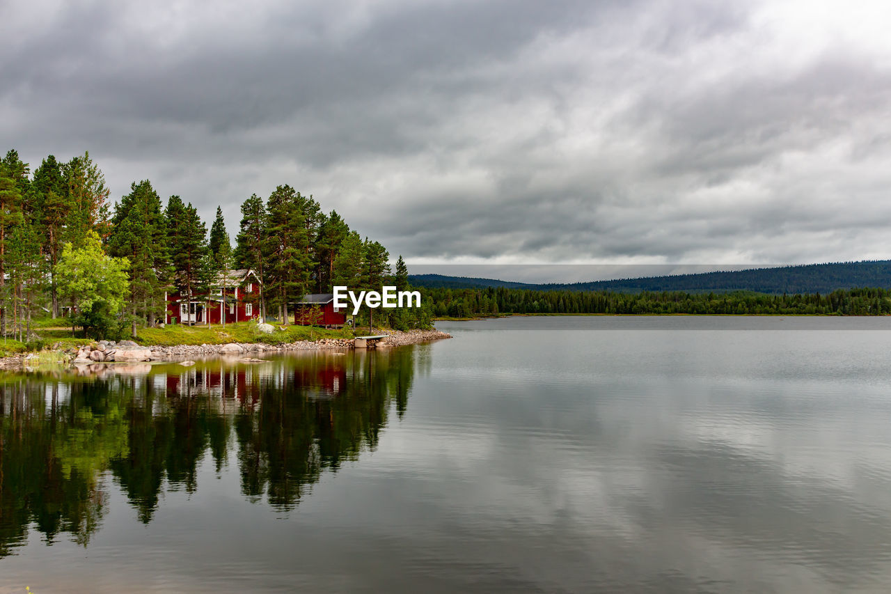 Red houses on the shore of a swamp with reflection in the water and sky storm clouds