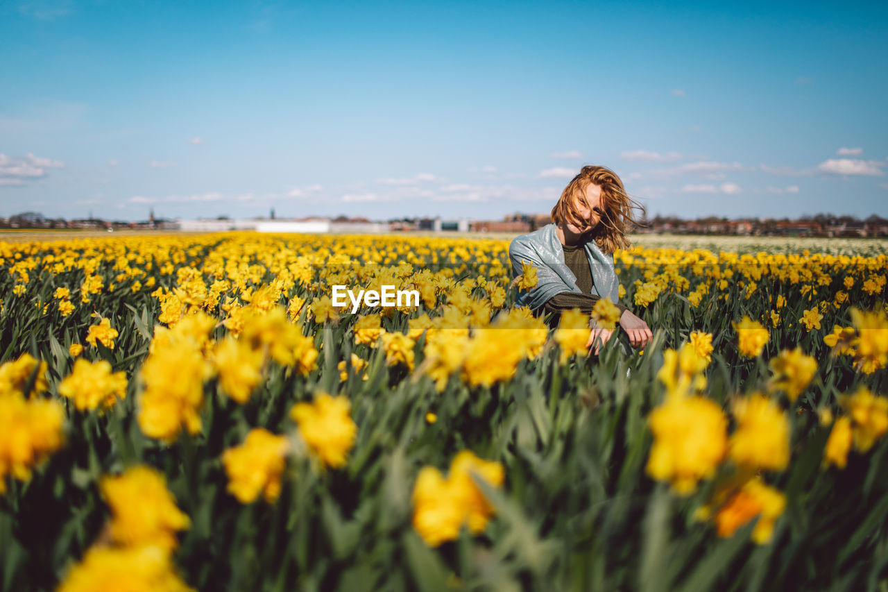 Scenic view of girl sitting on a narcissus field against sky