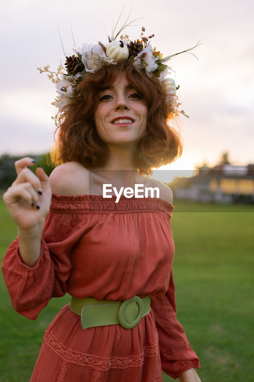 Portrait of woman wearing flowers while standing on land against sky during sunset