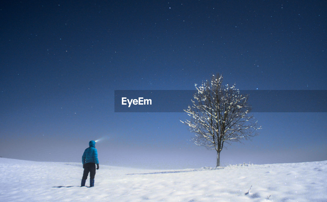 Rear view of man standing on snow against sky at night