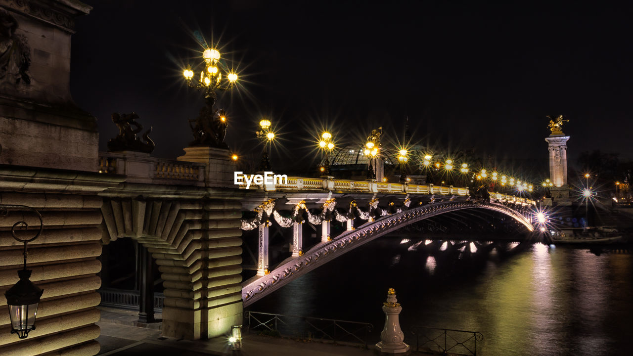 Illuminated pont alexandre iii over seine river against sky in city at night
