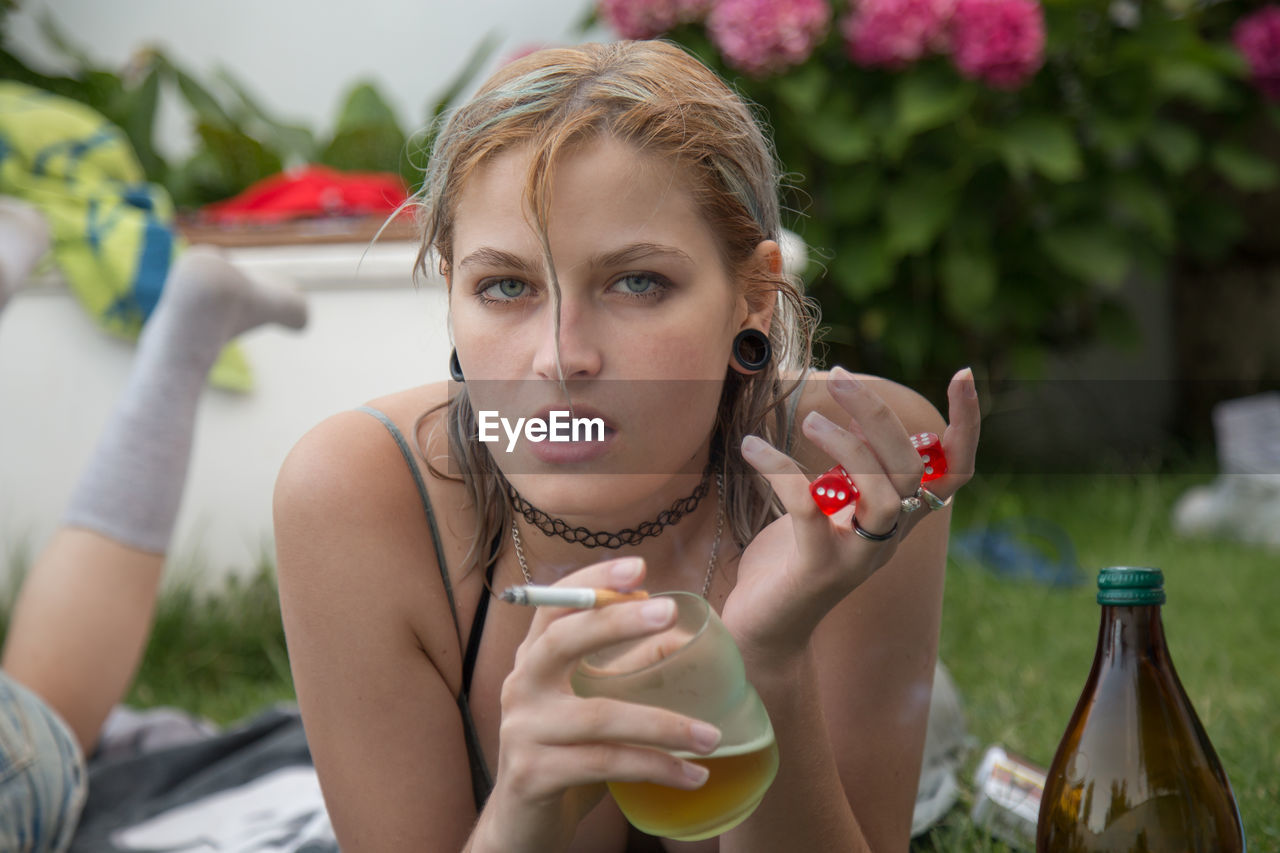 Portrait of young woman with cigarette and beer glass relaxing in park