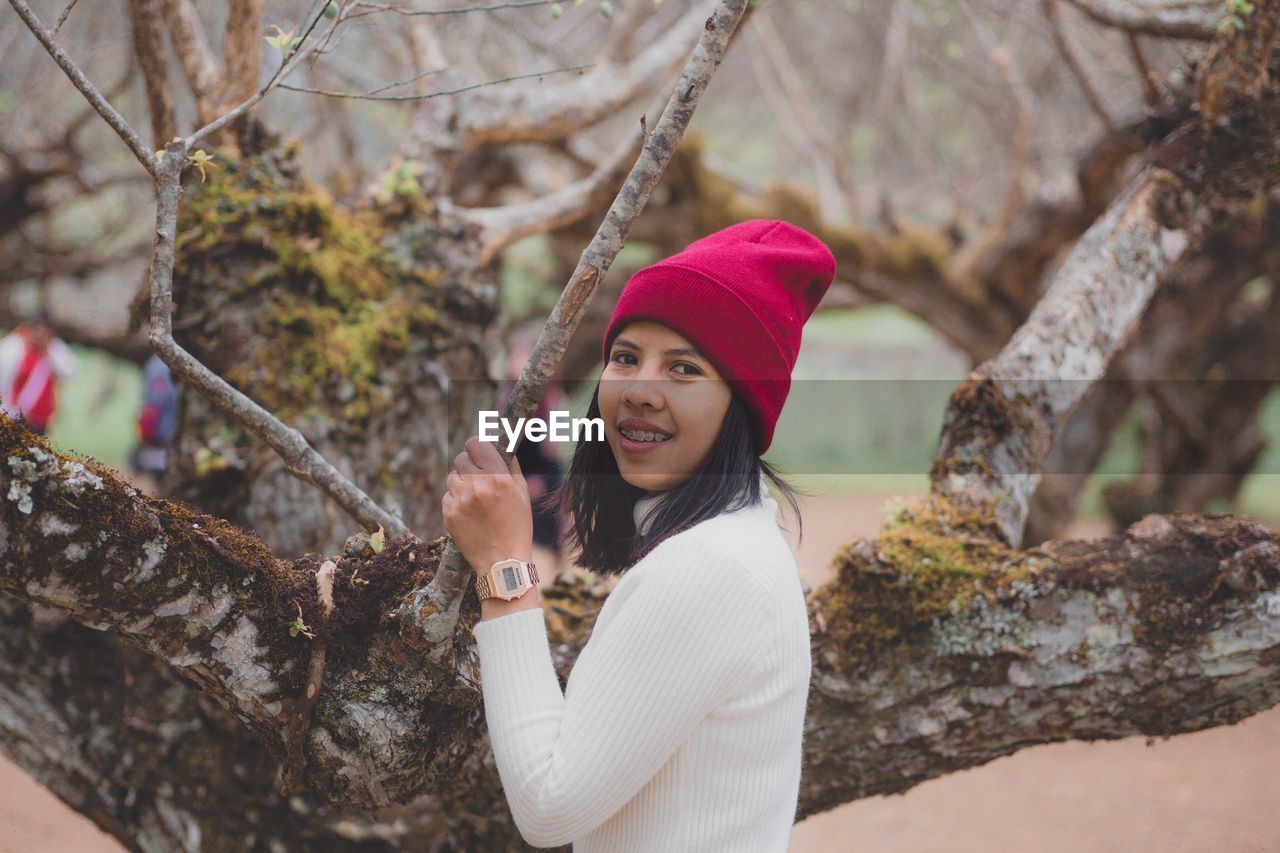 Portrait of woman wearing hat while standing against tree