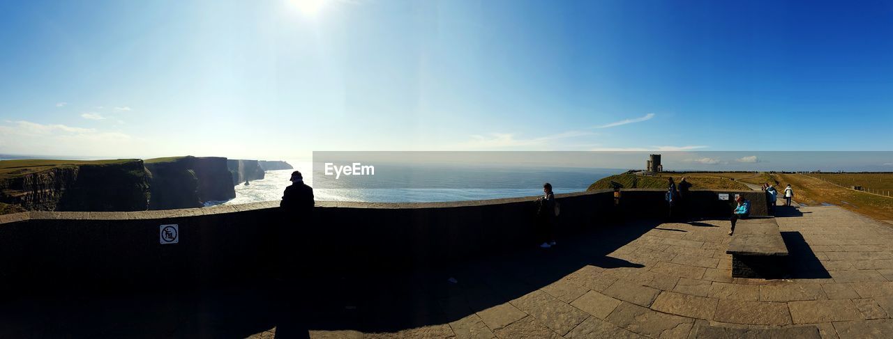 People at cliffs of moher against sea on sunny day