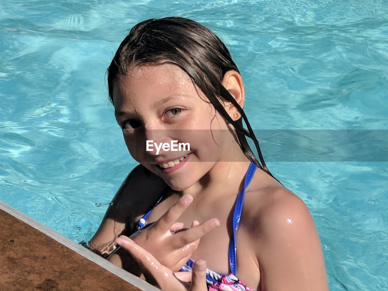 High angle portrait of smiling girl showing peace sign while swimming in pool