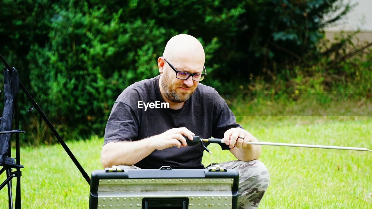 Man adjusting fishing rod at grassy field