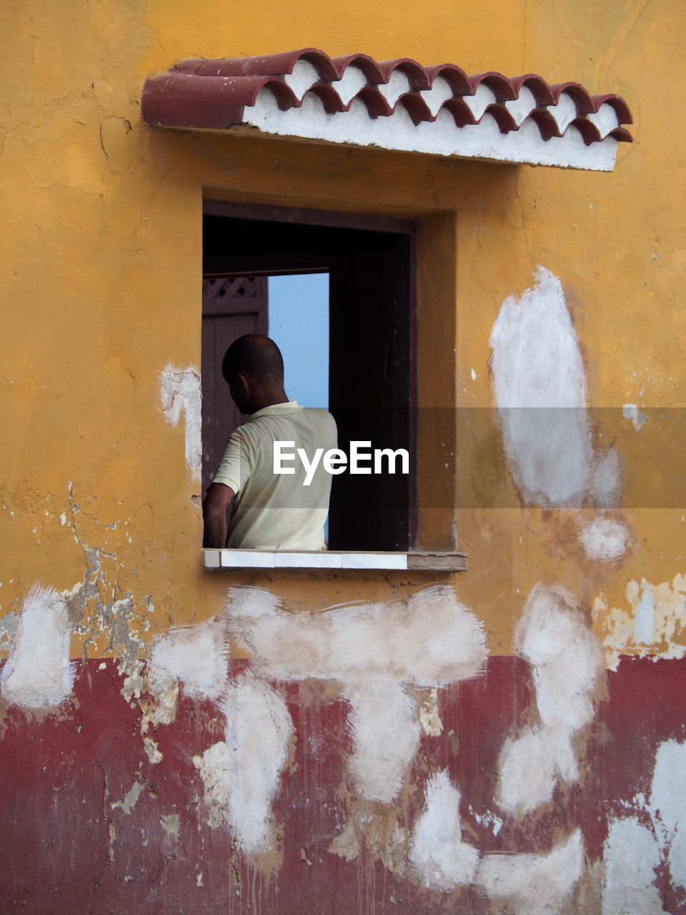 REAR VIEW OF WOMAN BY WINDOW AGAINST WALL