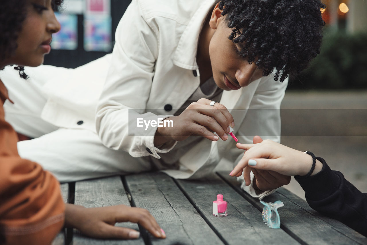 Teenage boy applying pink nail polish to female friend at table