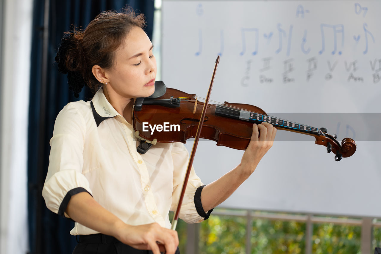 Mature woman practice playing violin in classroom