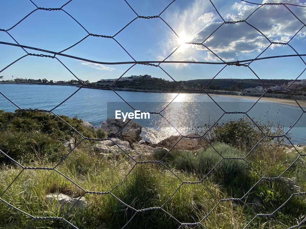 sky, water, nature, fence, sea, no people, beauty in nature, chainlink fence, wire, security, plant, tranquility, cloud, protection, land, scenics - nature, reflection, outdoors, beach, day, grass, tranquil scene, environment, wire fencing, sunlight, wire mesh, architecture, blue