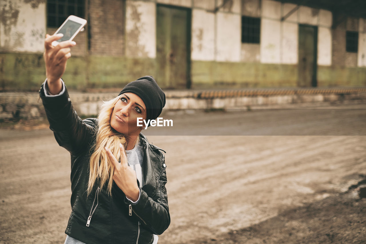 PORTRAIT OF YOUNG WOMAN USING PHONE WHILE STANDING ON CAMERA