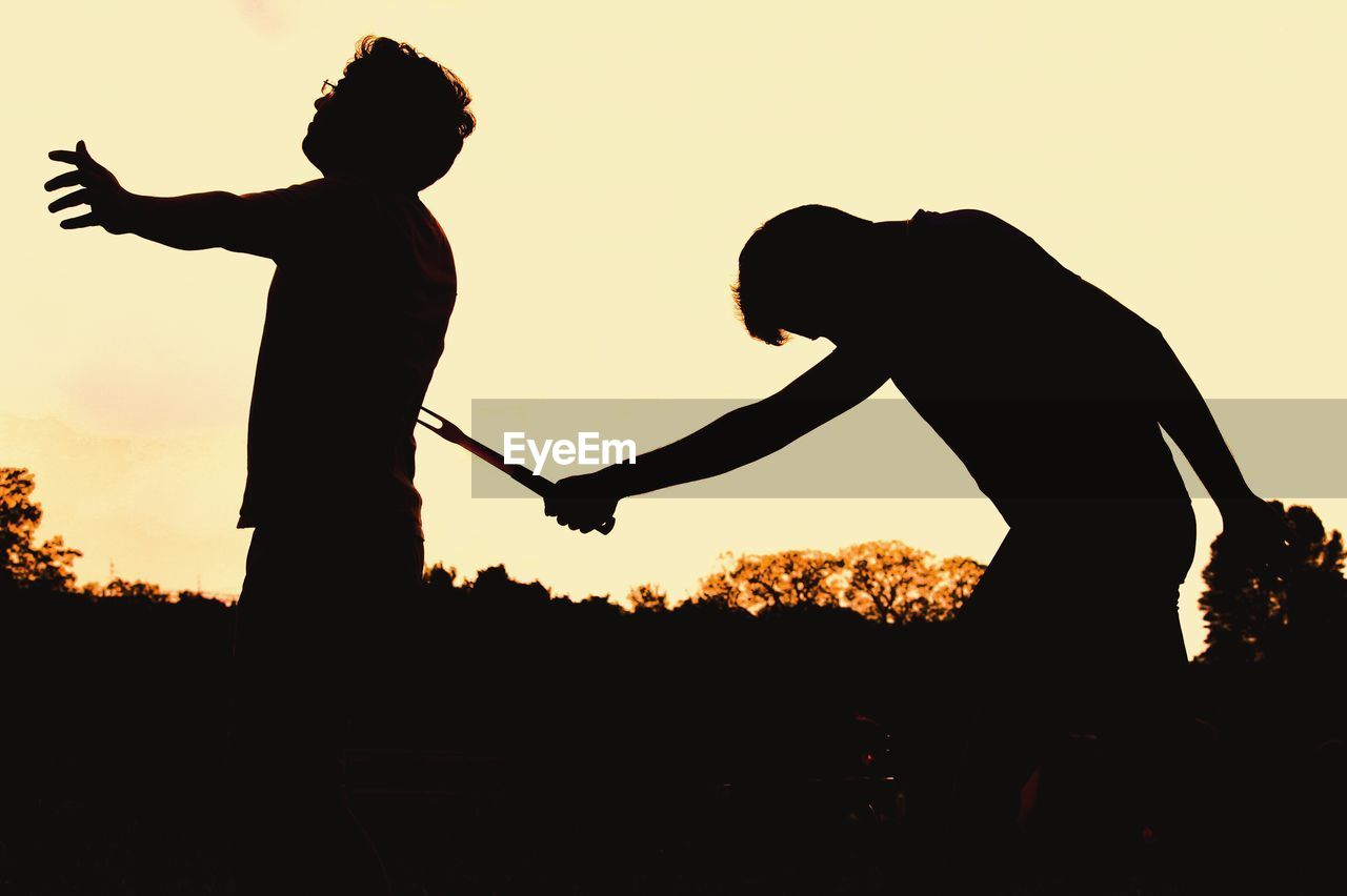 Silhouette murderer killing man against clear sky during sunset