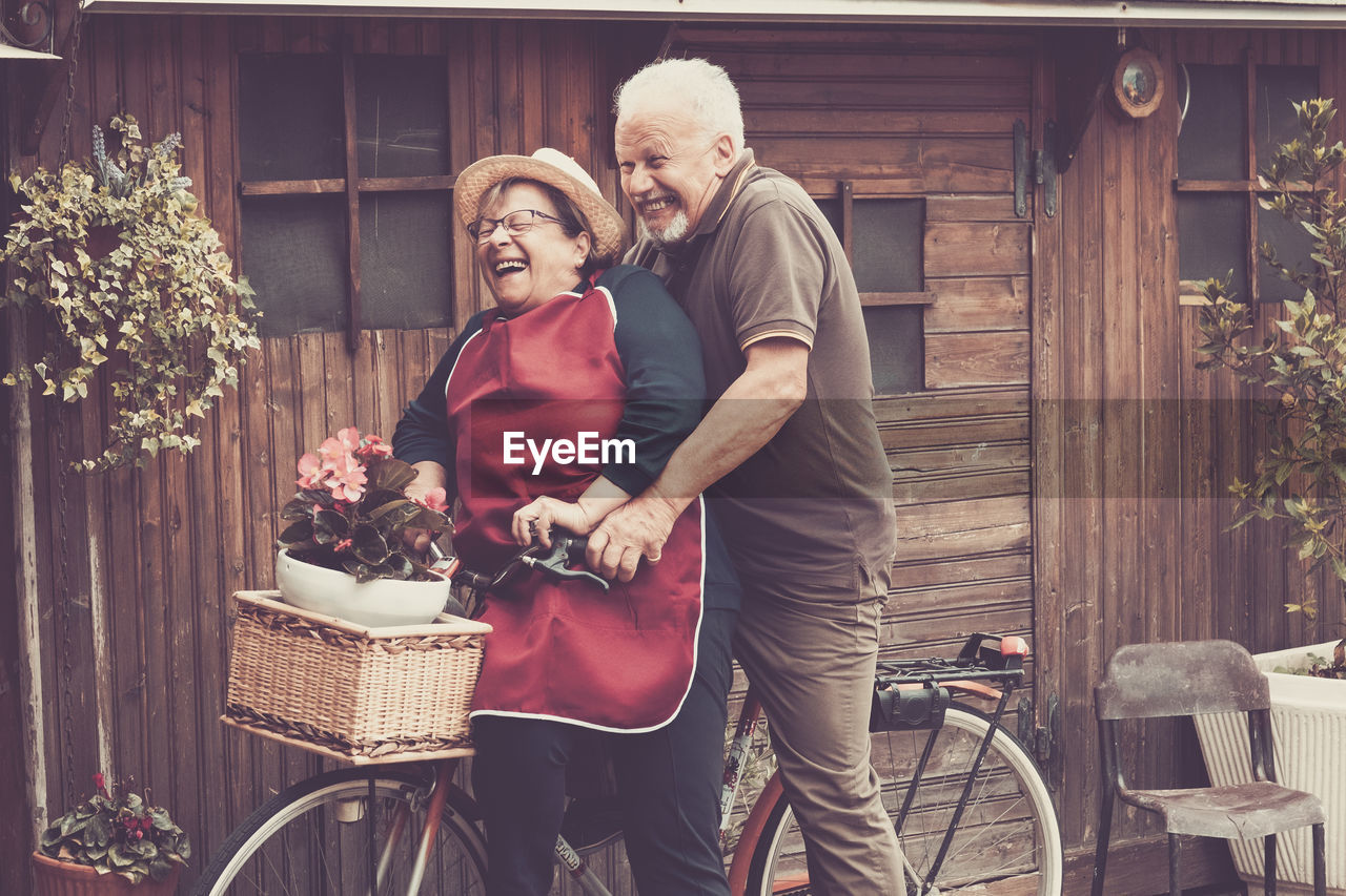 Happy senior couple riding bicycle by house