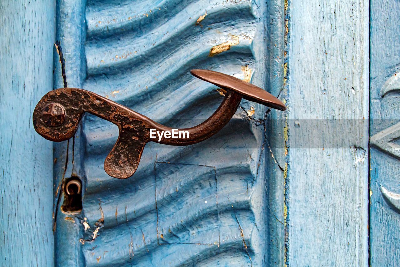 Close-up of rusty handle on blue door