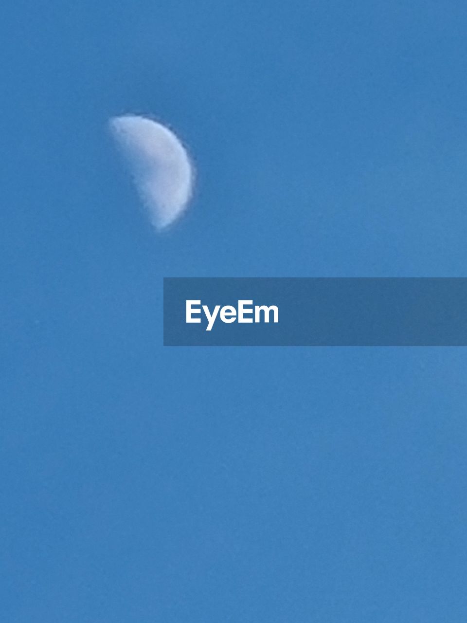 LOW ANGLE VIEW OF HALF MOON AGAINST BLUE SKY