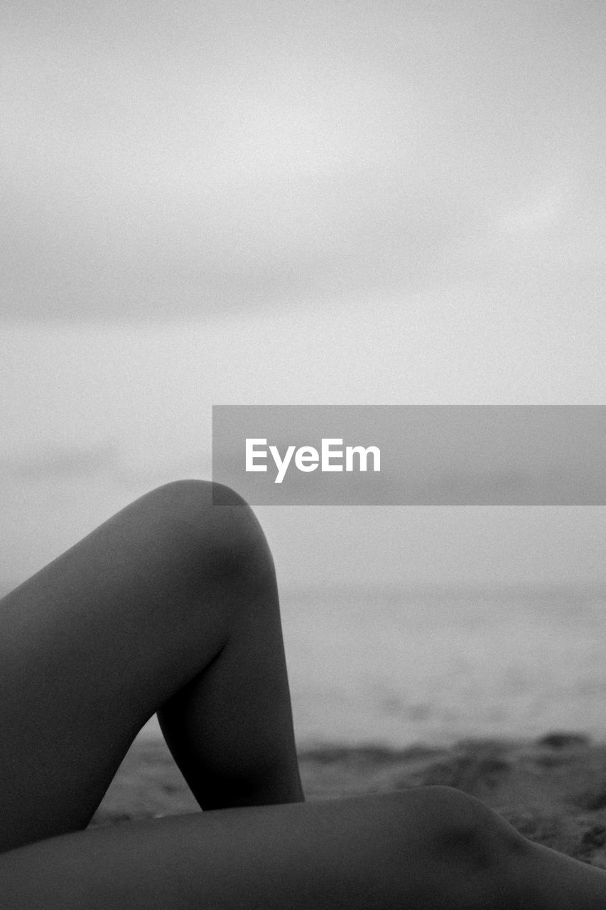 Midsection of woman at beach against cloudy sky