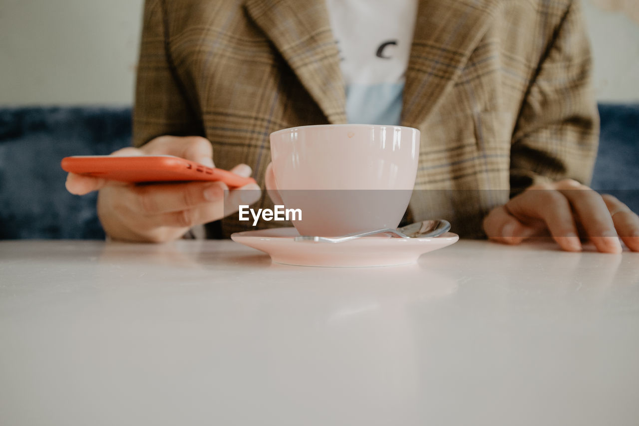 MIDSECTION OF WOMAN HOLDING COFFEE CUP WITH SPOON AND TABLE