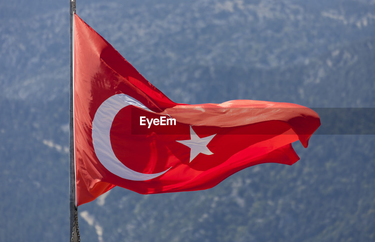 Close-up of red flag waving against mountains