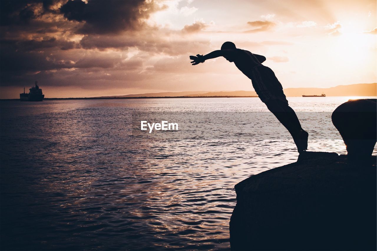 Silhouette man jumping in sea against sky during sunset