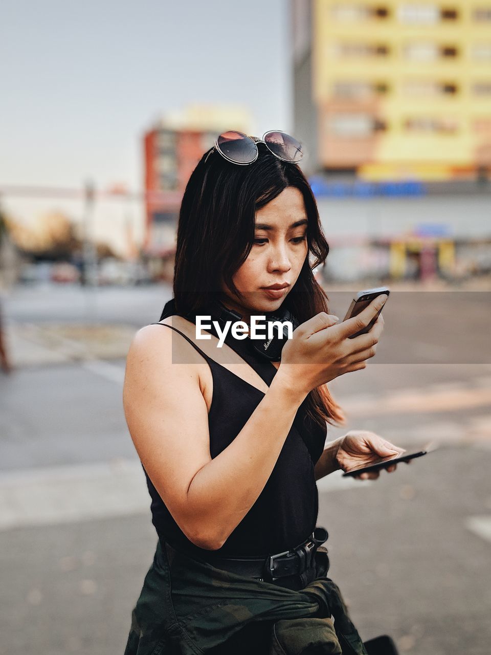 YOUNG WOMAN USING PHONE WHILE STANDING ON STREET IN CITY