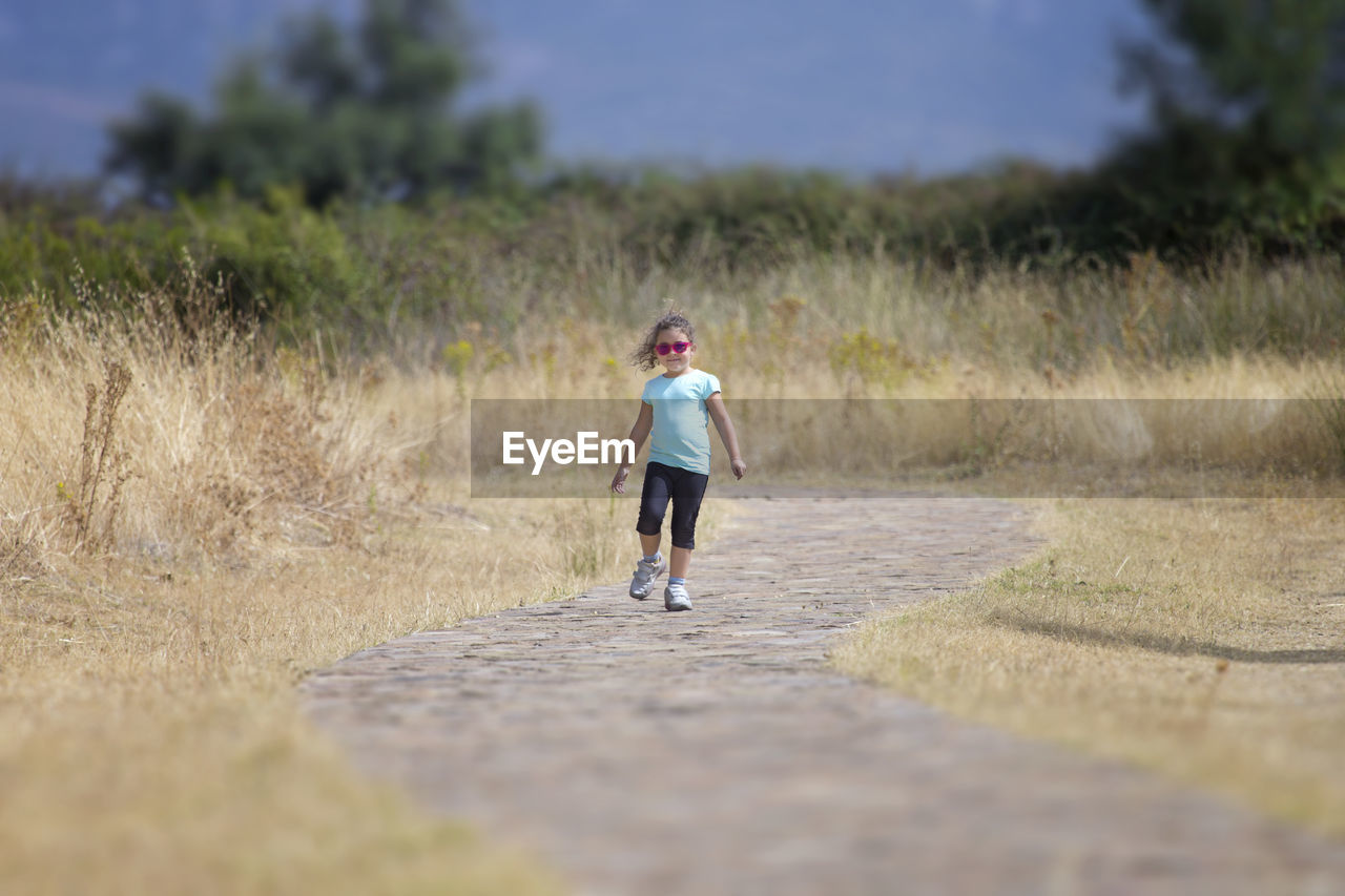 Full length of girl walking on road amidst grassy field against sky