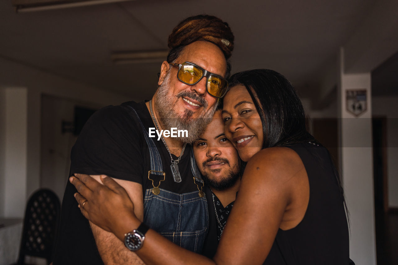 Smiling adult multiracial friends in casual clothes embracing while standing together and looking at camera