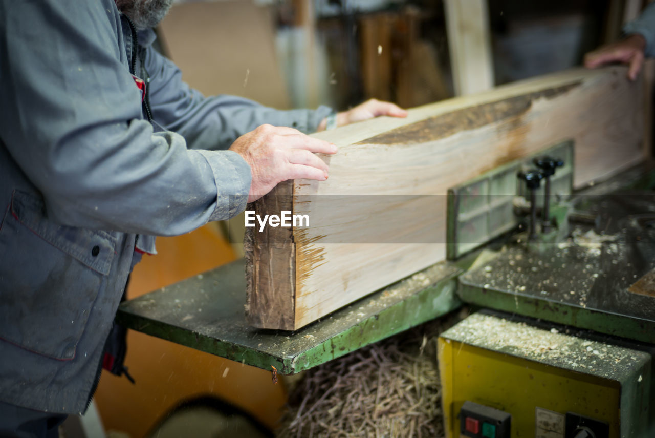 Midsection of carpenter cutting wooden plank at workshop