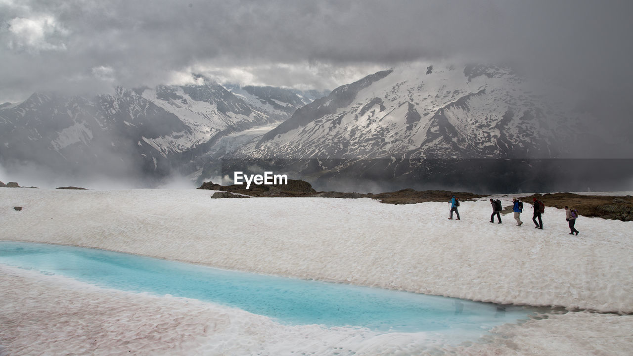 People walking on snow covered hill against cloudy sky