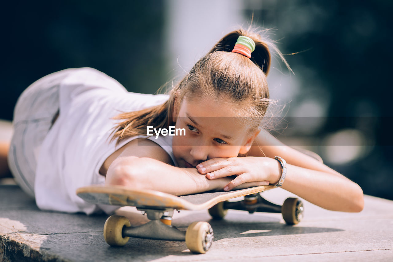 Portrait of cute girl sitting outdoors on skateboard