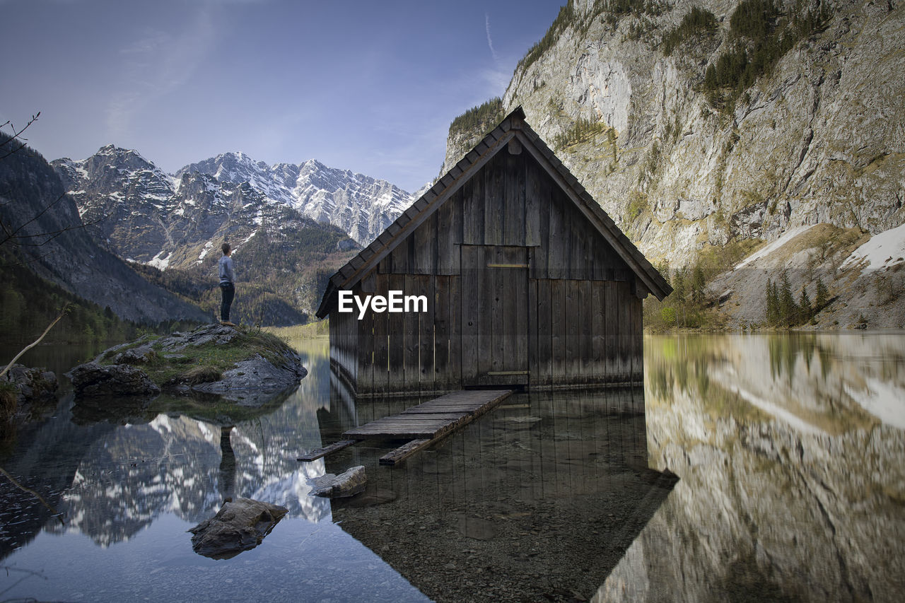 Man standing on rock by house in lake against sky