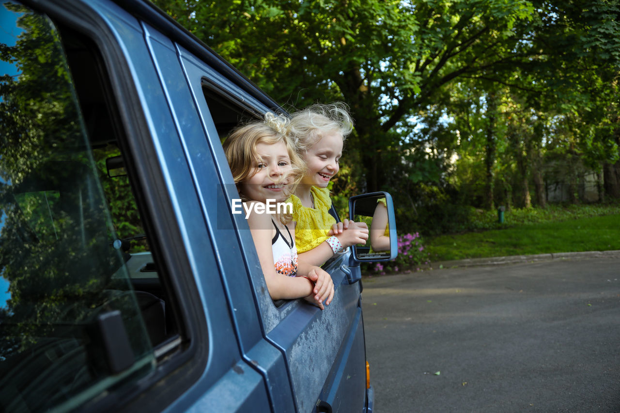 Two young girls smiling and leaning out of car window