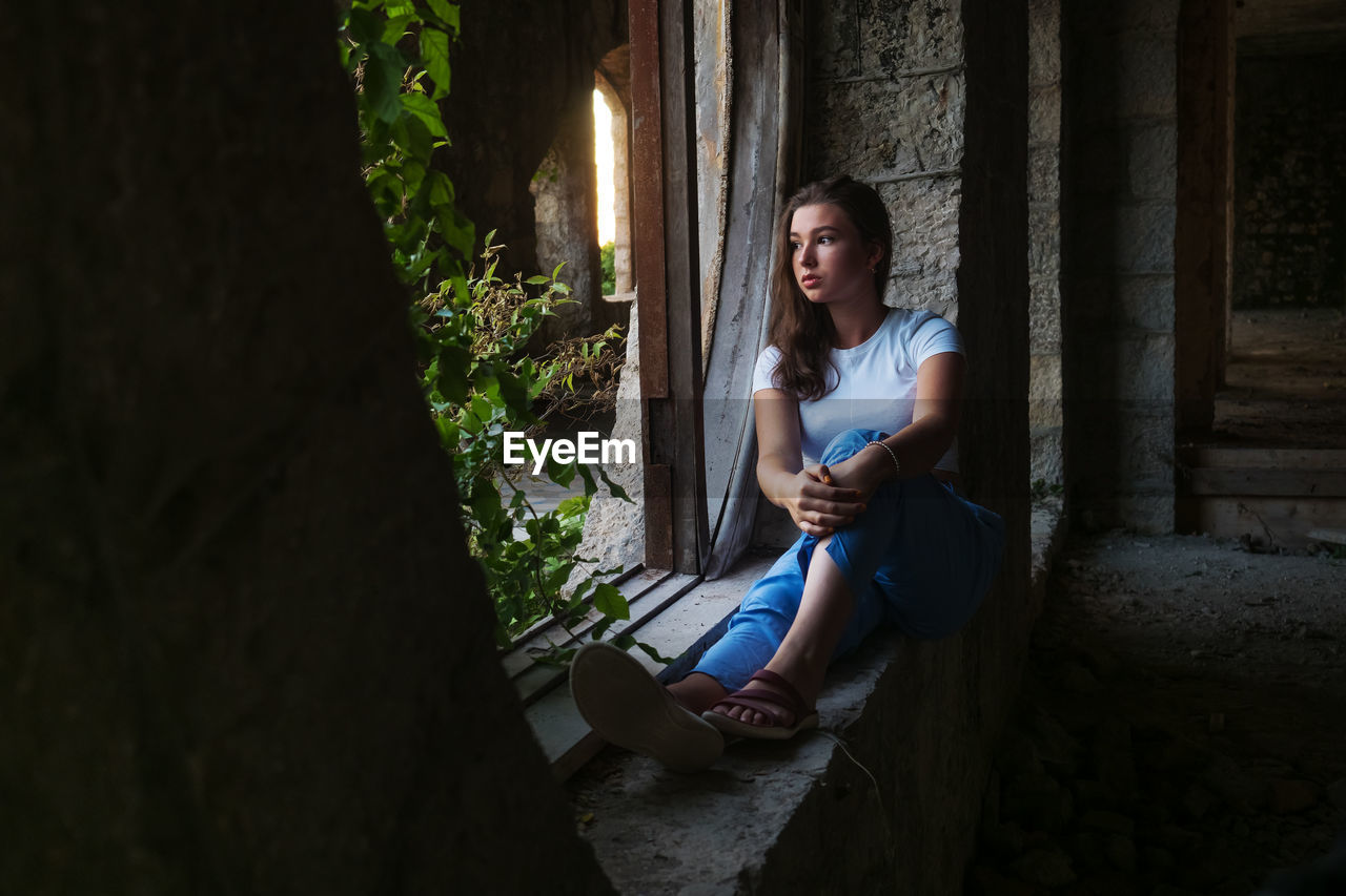 Teen girl sitting by the window in an abandoned building