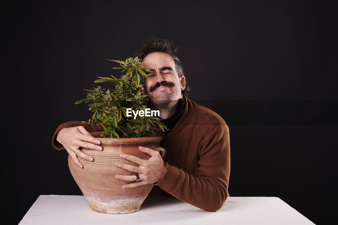 one person, adult, houseplant, black background, studio shot, men, plant, indoors, flowerpot, beard, potted plant, facial hair, portrait, growth, nature, copy space, lifestyles, person, holding, table, food and drink, front view, herb