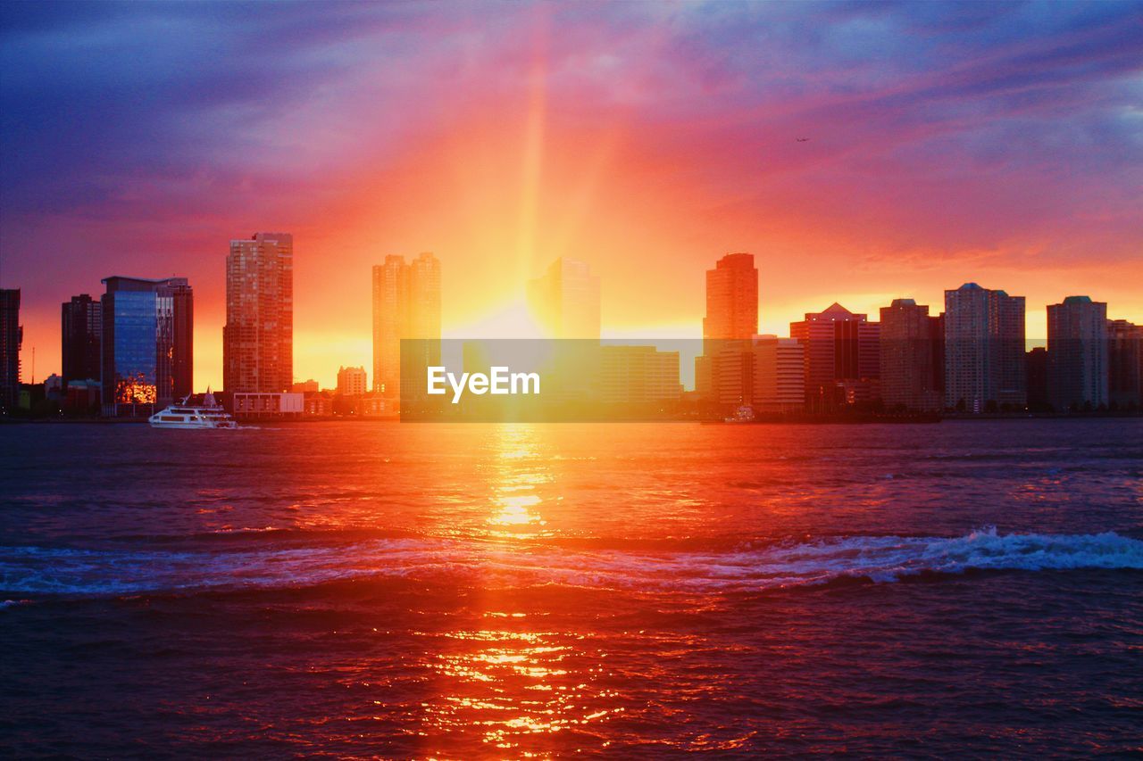 Sea with buildings in background at sunset